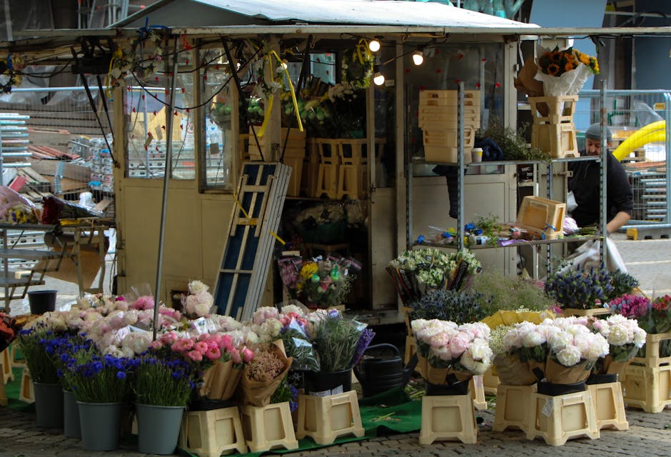 A market stall at Lewisham Market, featuring an array of fresh flower bouquets and floral arrangements. The flowers include pink peonies, white roses, purple asters, and blue hydrangeas, all displayed