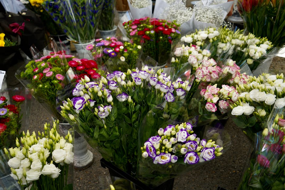 An assortment of fresh flowers arranged in bouquets and potted displays on a florist's table, featuring white Lisianthus with delicate, ruffled petals, purple and white Eustoma (Lisianthus) with tight